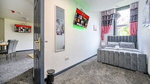 A bedroom with a bed, a window with curtains, a wall-mounted TV, and a dining area with chairs and a table. - Stylish Ground Floor Apartment in West Yorkshire (West Yorkshire)