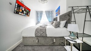 Ein modernes Schlafzimmer mit einem großen Bett, einem an der Wand montierten Fernseher, der Netflix zeigt, einer Deckenleuchte und einem Fenster mit Vorhängen.