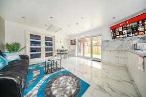 Una sala de estar moderna con sofá, una mesa de centro y una pared con televisión mostrando Netflix.