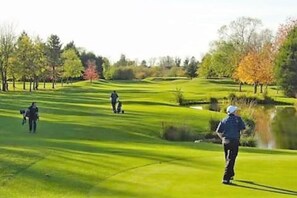 Um campo de golfe com lago, árvores e jogadores.
