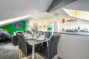 Uma sala de jantar moderna com mesa de vidro, cadeiras pretas e uma parede verde de destaque.
