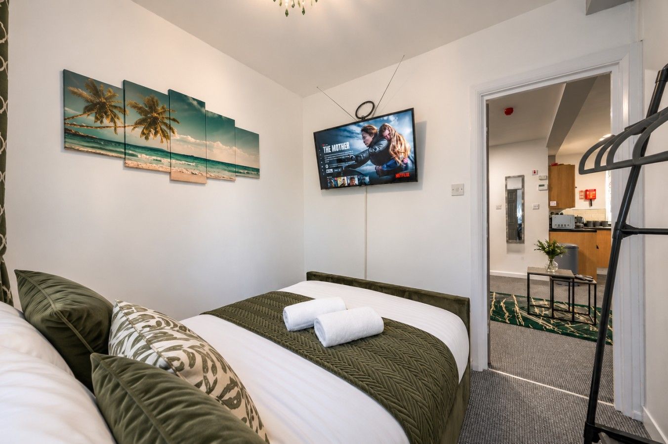 Une chambre d’hôtel avec un lit, des oreillers, un téléviseur fixé au mur et une vue sur la cuisine et le couloir.