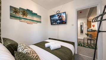 Une chambre d’hôtel avec un lit, des oreillers, un téléviseur fixé au mur et une vue sur la cuisine et le couloir.