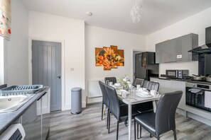 A modern kitchen with a dining area, a gray trash bin, and a fruit-themed wall art. - *16PT* For your relaxed & Cosy stay + Free Parking (Armley)