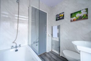 Ein modernes Badezimmer mit Duschkabine aus Glas, einer weißen Badewanne, einem weißen Waschbecken und zwei Handtuchhaltern an der Wand.