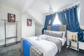 Ein Schlafzimmer mit einem Bett, einem Nachttisch, einem Fenster mit Vorhängen, einer Chandelier und Wandbildern.