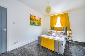 A bedroom with a bed, a painting, a window with yellow curtains, and a chandelier. - *16PT* For your relaxed & Cosy stay + Free Parking (Armley)