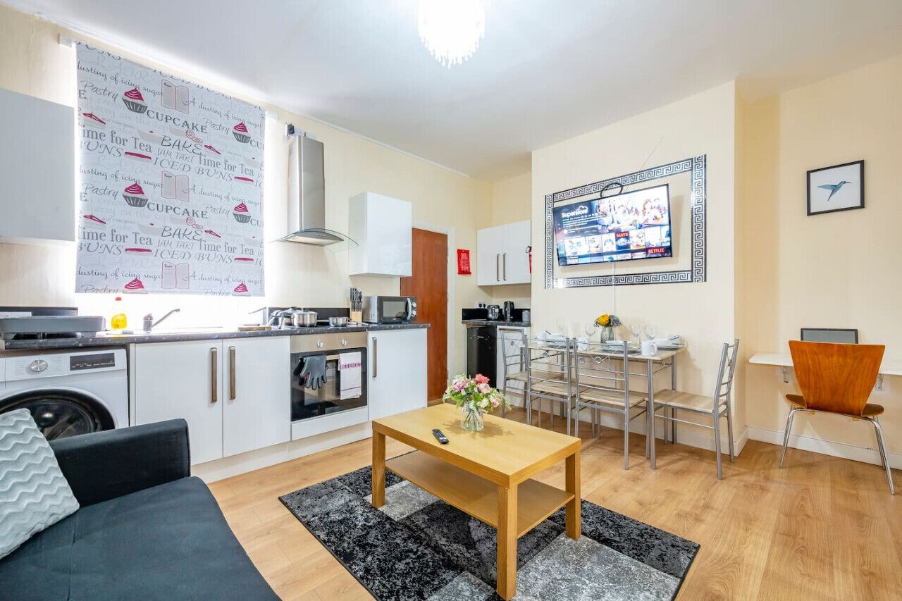 A compact living space with a kitchenette, a dining area, and a TV mounted on the wall.