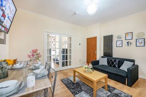 Un salon comprenant un canapé, une table basse, une table à manger avec ses chaises, et une porte donnant sur une autre pièce.