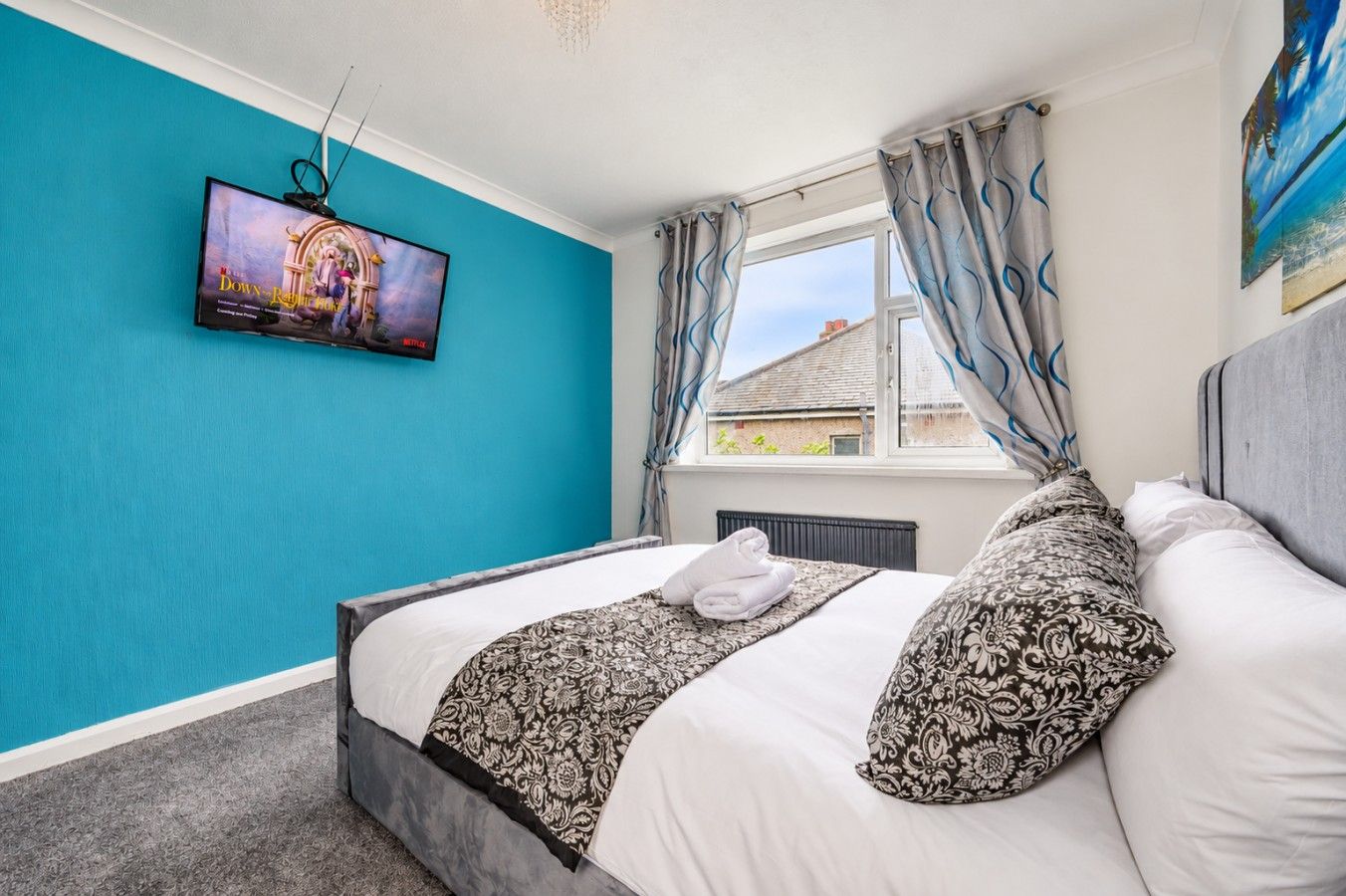 Une chambre d’hôtel avec un lit, un téléviseur fixé au mur, une fenêtre avec des rideaux et une vue sur l’extérieur.