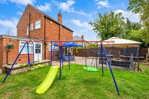 A backyard with a swing set, a slide, a trampoline, and a barbecue area. - Stylish Family Home with Hot Tub (West Yorkshire)