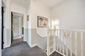 A hallway with a glass shower door, a staircase with white balusters, and a framed picture on the wall. - Stylish Family Home with Hot Tub (West Yorkshire)