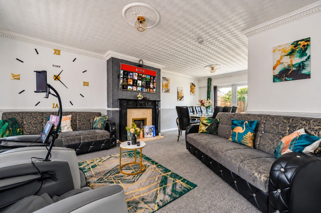 A spacious living room with a fireplace, a mounted clock, and a bookshelf with various items.