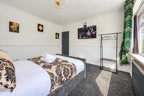 A hotel room with a bed, a TV, a coat rack, and a window with curtains. - Stylish Family Home with Hot Tub (West Yorkshire)