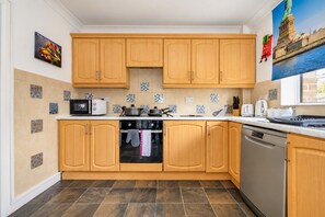 A kitchen with wooden cabinets, a microwave, a stove, and a dishwasher. - Stylish Family Home with Hot Tub (West Yorkshire)