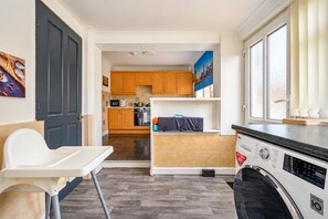 A compact kitchen with wooden cabinets, a microwave, and a washing machine. - Stylish Family Home with Hot Tub (West Yorkshire)