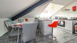 A modern kitchen with a central island, a dining area with grey chairs, and a kitchen counter. - Stylish Home with Free Parking (West Yorkshire)