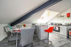 Een moderne keuken met een centraal eiland, een eetgedeelte met grijze stoelen en een keukentrap.