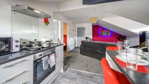 A modern kitchen with a dining area, a visible oven, and a red accent wall. - Stylish Home with Free Parking (West Yorkshire)