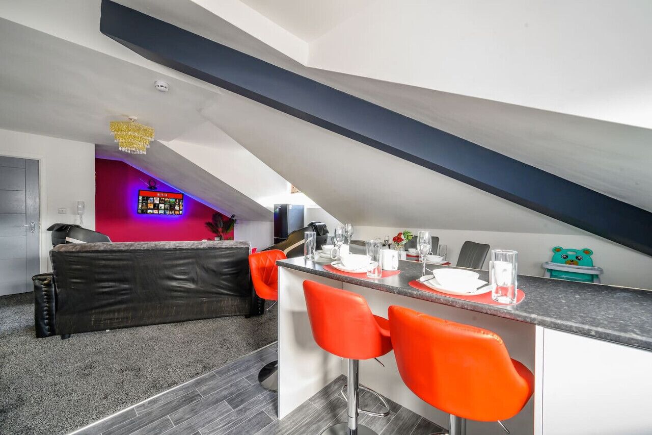 Una cocina moderna con barra, una mesa de comedor para cuatro personas y una pared roja decorativa.