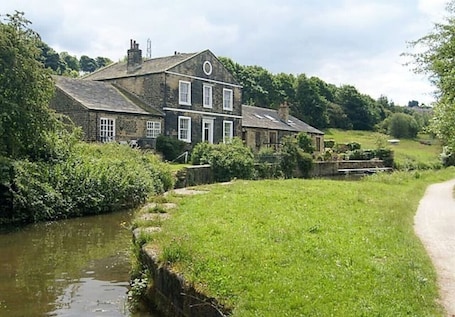 A two-story stone house with a river in front, surrounded by greenery.. *F19GH* For relaxed & Cosy stay/Free Parking/WiFi