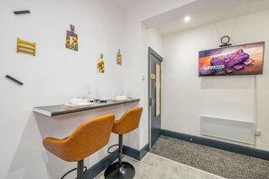 Une chambre d’hôtel moderne dotée d’un coin bar, de deux tabourets de bar, d’un téléviseur à écran plat et d’œuvres d’art décoratives murales.