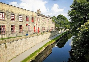 Een stenen gebouw met rode deuren en ramen, met een kanaal ernaast en een gazon ervoor.