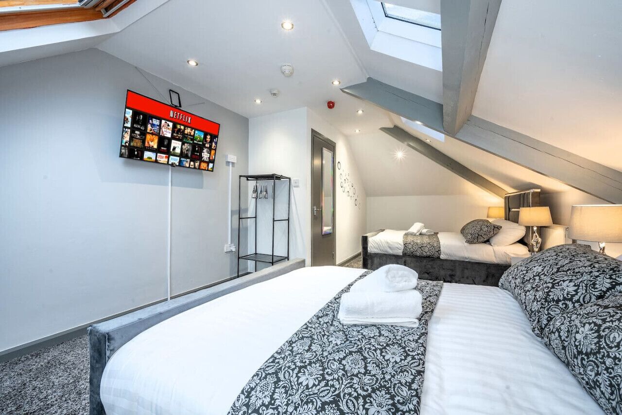 A modern hotel room with a large bed, a television displaying Netflix content, a shower area, and a skylight.