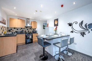A modern kitchen with wooden cabinets, a central island with bar stools, and a decorative wall mural. - *F4GH for your most relaxed & Cosy stay + Parking (West Yorkshire)