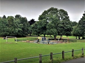 Een park met een speeltuin, een voetbalkooi en bomen.