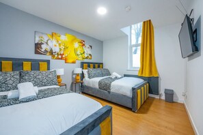 A hotel room with two beds, a large window with yellow curtains, a flat-screen TV, and a painting on the wall. - *F18GH* For relaxed & Cosy stay/Free Parking/WiFi (West Yorkshire)