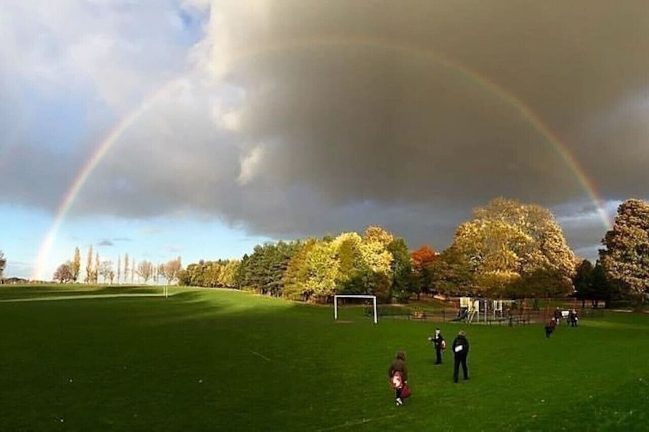 A grassy field with a goalpost, trees, and a rainbow.