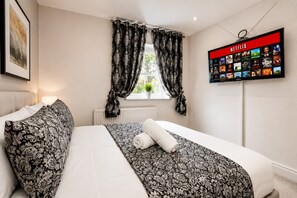 Ein Hotelzimmer mit einem Bett, einem Vorhangfenster, einem an der Wand befestigten Netflix-Bildschirm und einem Heizkörper.