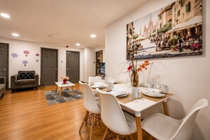 Een eetgedeelte met een tafel voor vier personen, een bank en een schilderij van een straatbeeld.