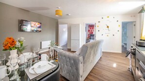 Een moderne woonkamer met een grijze bank, een eethoek met een glazen tafel, en een keuken met een fornuis.