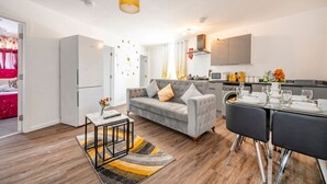 Een moderne woonkamer met een bank, een eettafel gedekt voor twee personen en een keukenhoek met een magnetron en fornuis.