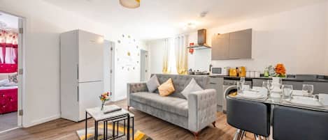 A modern living room with a sofa, a dining table set for two, and a kitchen area with a microwave and stove.
