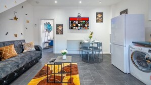 Un salon moderne avec un canapé, une table basse et un coin repas avec des chaises. On y trouve également un lave-linge et un réfrigérateur.
