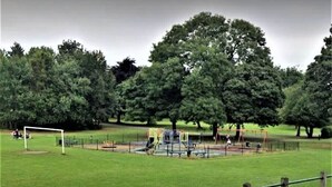 Un parc avec une aire de jeux, un but de football et des arbres.
