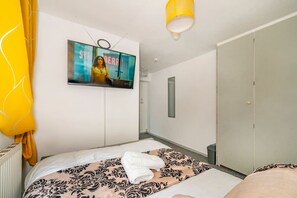 Una habitación de hotel con cama, televisor montado en la pared, armario y una lámpara colgante amarilla.