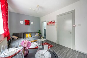 A modern living room with a gray sofa, a dining table set for four, and a red and white patterned rug. - *F6*GH* Setup for your most rela (West Yorkshire)