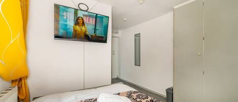 A hotel room with a bed, a television mounted on the wall, a wardrobe, and a yellow hanging lamp.