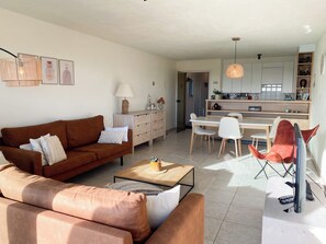 Ein Wohnzimmer mit braunem Sofa, einem Couchtisch und einem Essbereich mit weißem Tisch und Stühlen.