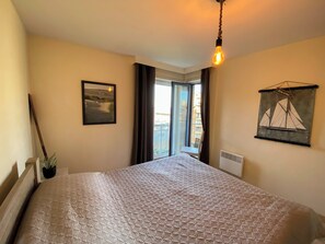 Ein Schlafzimmer mit einem Bett, einem Bild an der Wand, einem Fenster mit Vorhängen und einer Pendelleuchte.