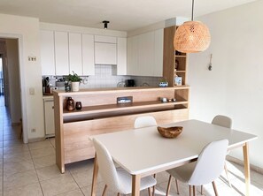 Eine moderne Küche mit weißen Schränken, einer Holztischinsel und einem Essbereich mit weißem Tisch und Stühlen.