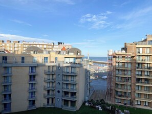 Ein mehrgeschossiges Wohngebäude mit Balkonen, Blick auf das Meer und einem Pier im Hintergrund.