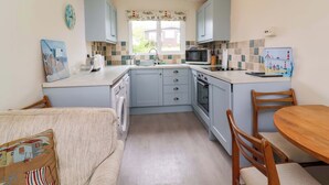A compact kitchen with a dining area, featuring a microwave, toaster, sink, and a small oven. - Sea Breeze (Bideford)