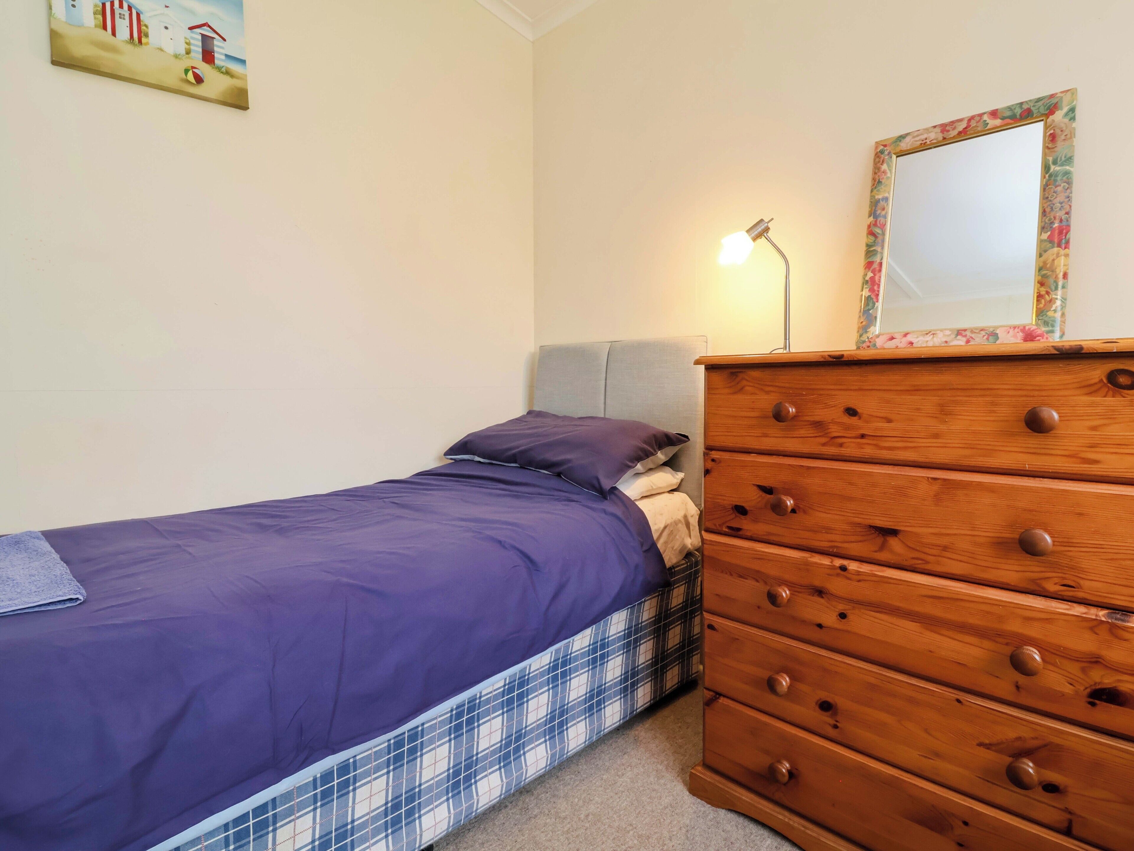 A bedroom with a bed, a dresser, a lamp, and a painting on the wall.