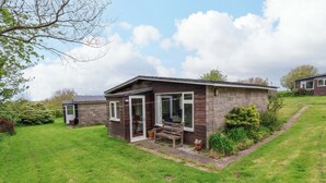 A small, single-story building with a porch and a bench, surrounded by a grassy yard and a stone wall. - Sea Breeze (Bideford)
