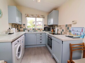 A compact kitchen with a washing machine, microwave, and sink. - Sea Breeze (Bideford)